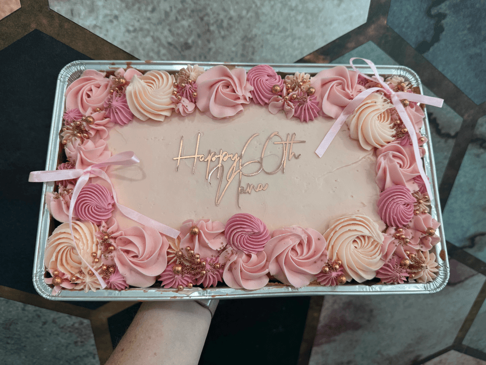 A pink sheet cake reading Happy 60th.