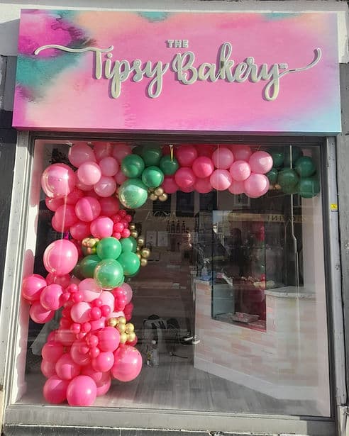 The Sidcup shopfront with a pink and teal watercolour fascia and a pink, green and gold balloon arch.